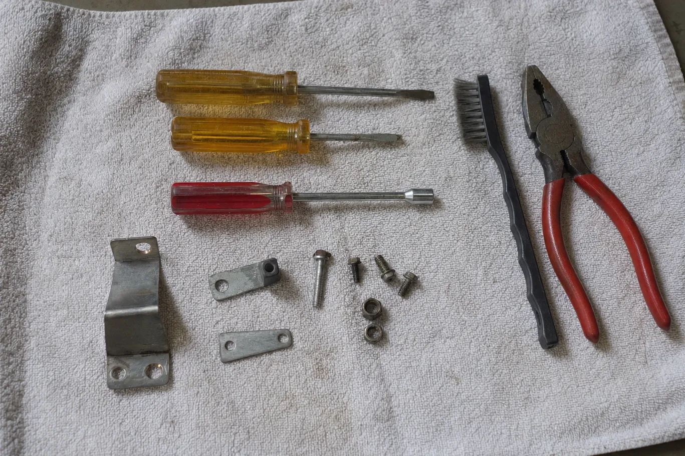 Flat drivers, a nut driver, wire brush and linesman pliers on a towel with an L-bracket and link plates